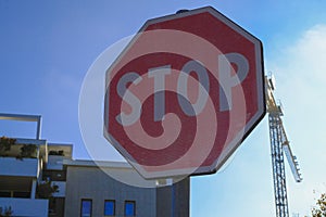 Stop sign close-up against buildings, building crane, blue sky. Transportation, road signs