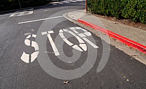 Stop sign painted on asphalt of red curb street at intersection