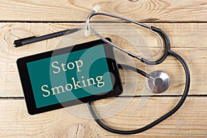 Stop Smoking - Workplace of a doctor. Tablet, medical stethoscope, black pen on wooden desk background. Top view