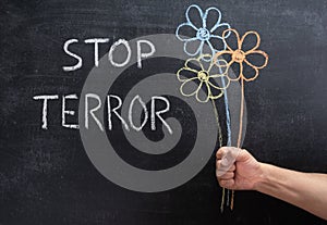 STOP TERROR on a chalkboard, three flowers drawn in chalk in a man`s hand