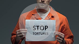 Stop tortures phrase on cardboard in hands of Caucasian prisoner, protest
