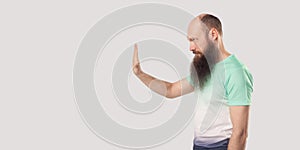 Stop, wait. Profile side view portrait of serious middle aged bald bearded man in green t-shirt standing with stop hand gesture