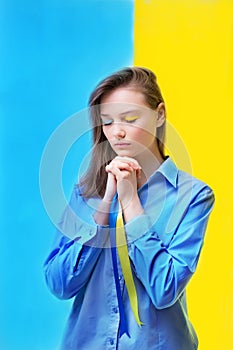 Stop war. Girl closing her eyes will hold a yellow-blue ribbon on the background of the Ukrainian flag.