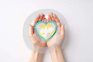 Stop the war in Ukraine concept. Top overhead view photo of female hands holding yellow and blue heart with white dove silhouette