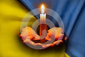 Stop the war in Ukraine. A girl with a candle in her hands prays against the background of the flag of Ukraine, War in Ukraine, a