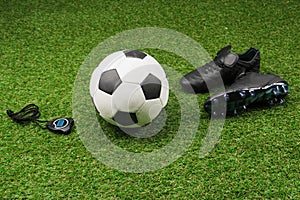 Stopwatch with soccer ball and boots on grass pitch