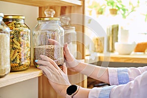 Storage of food in the kitchen in pantry, woman& x27;s hands with jar of buckwheat