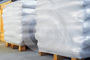 Storage of packaged goods or cargo in warehouse. On wooden pallets there are bags of cement wrapped with polyethylene