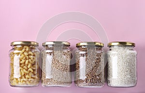 Storage of rice, buckwheat, wheat groats and pasta in glass jars. Crisis food stock for quarantine isolation period on pink