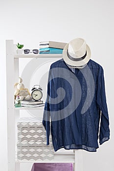 Storage system in the bedroom. Shelving with boxes, alarm clock, books, for small items and with dress hanging on a hanger