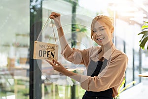 Store owner turning open sign broad through the door glass and ready to service. Happy asian female small business