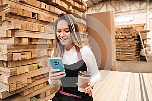 Store seller looking at mobile phone during break of work at wood warehouse