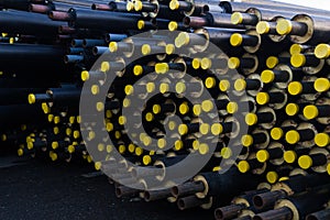 Stored many black steel pipe with heat insulation on construction site in a plastic tube wrapper lying with yellow lids pipes