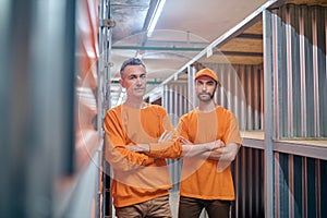 Storehouse worker and his coworker standing among storage containers