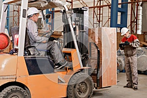 The storekeeper marks the arrival on the tablet. man driving a forklift through a warehouse in a factory. driver in