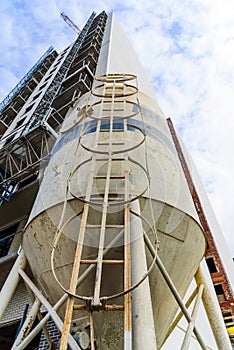 Storing sand in a silo next to the scaffolding of a building construction site