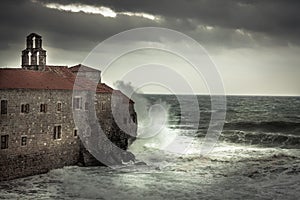 Storm with big stormy waves at coastline crashing on the walls of a medieval castle on sea shore and dark dramatic sky in fall se