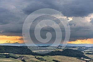 Storm cloud building up from afar during sunset over agricultural landscape in Tuscany, Italy