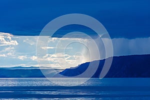 Storm cloud over lake Baikal with sun light and rain. Mountains in the fog, waves on the water, clouds and blue tones of the