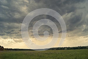 Storm cloud over yellow green fields forests and hills