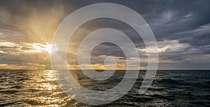 Storm clouds with the sun setting and sun rays over the ocean.