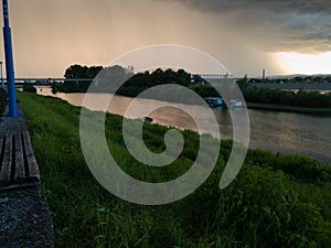 Storm cumulonimbus cloud with heavy rain or summer shower, severe weather and sun glow behind rain. Landscape with Sava river with