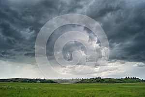 Storm cyclone over summer fields, hills and forests