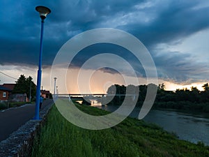 Storm dark cloud with heavy rain or summer shower, severe weather and sun glow behind rain. Landscape with Sava river and