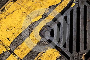 Storm drain and yellow road markings on the old asphalt