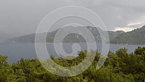 A storm with rain, thunderstorm and lightning looming on the Mediterranean Sea coast with mountains covered with forests near the