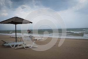 Storm on the sea with thunderclouds. Beach umbrella and inverted sun beds under umbrella on the beach.