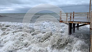 Storm on the sea. Waves cover the pier. Thunderclouds in the sky. Strong wind on the ocean. Autumn on vacation. Old