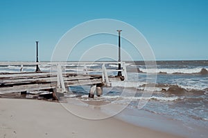 Storm sea waves empty wooden pier in dramatic blue sky background. Seascape with running splashing sea waves. Sandy
