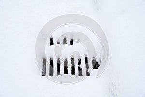 Storm sewer grate covered in fresh snowfall, cold winter day