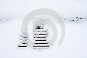 Storm sewer grate covered in fresh snowfall, cold winter day