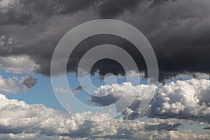 Storm sky. Dark grey and white big cumulus clouds on blue sky background texture, thunderstorm