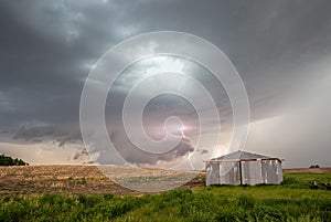 Storm and wall cloud with lightning bolt behind an old farm building.