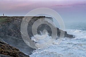 Storm waves crash onto the Cape Ajo in Spain with the lighthouse on the cliffs above at sunrise photo