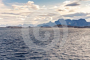 Stormclouds with sun shining through them above dramatic mountain range of Lofoten Islands, viewed from boat on the sea