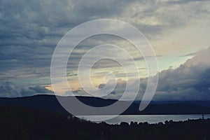 Stormy clouds over the lake and green forest in middle of day