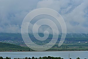 Stormy clouds over the lake and green forest in middle of day