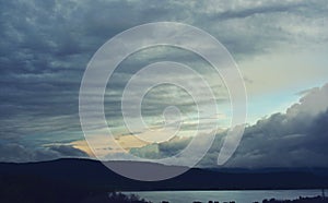 Stormy clouds over the lake and green forest in middle of day