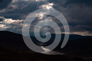 Stormy clouds with sunrays on a mountain lake at sunset