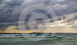 Stormy dark clouds above the sea with sandy beach and curling waves