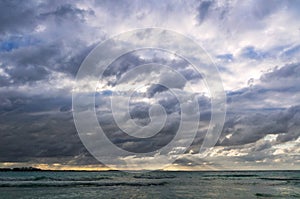 Stormy dark clouds above the sea with sandy beach and curling waves