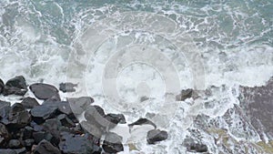 Stormy sea with foamy waves breaking in splashes against cliff, slow motion