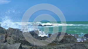 Stormy sea and water waves splashing on rocky beach on blue sky landscape. Water waves breaking on stony coast in ocean