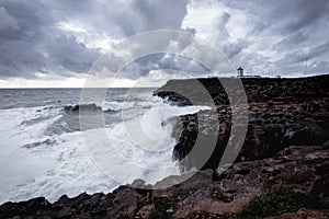 Stormy seascape and lighthouse on rocky coastline.