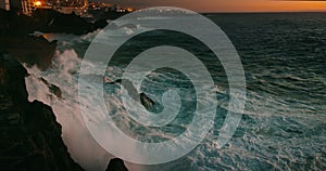 Stormy seaside at night coastal resort town Puerto de Santiago. Ocean waves crash on rocky dark volcanic beach at sunset