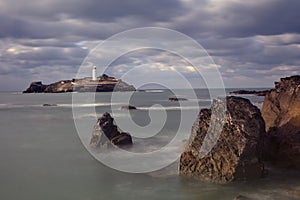 Stormy skies over Godrevy Lighthouse on Godrevy Island in St Ives Bay with the beach and rocks in foreground, Cornwall uk